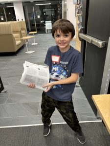 A young boy beams with pride as he holds up his completed assignment
