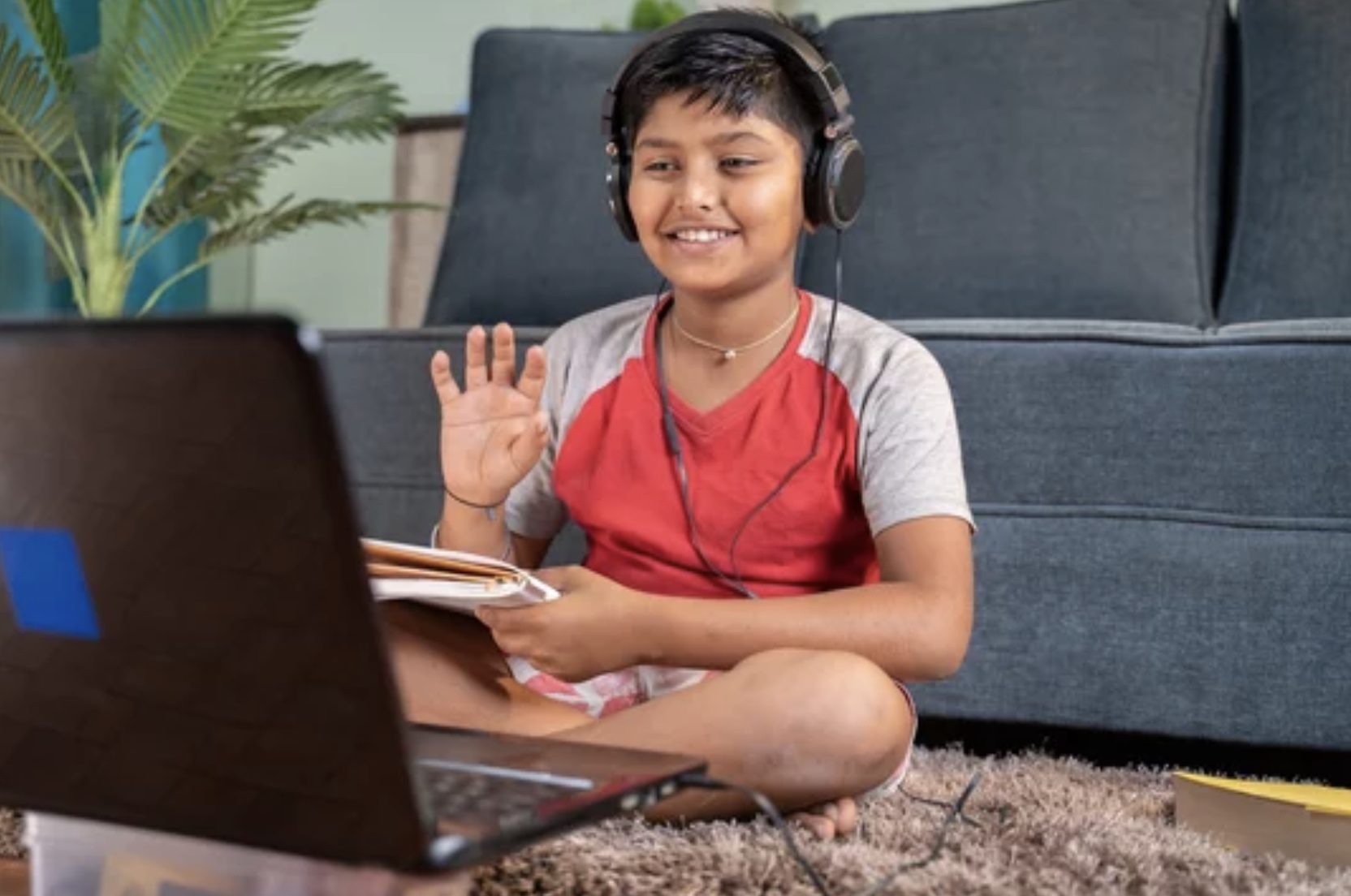 A smiling child with headphones waves at their virtual class, embracing remote learning